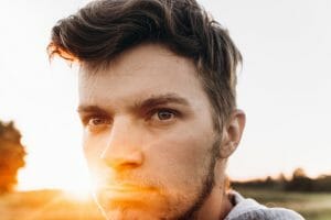 Stylish hipster man looking in sunlight in summer evening field