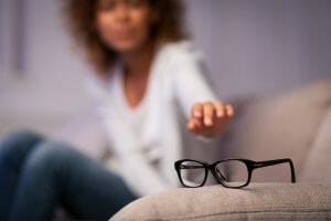 Eyesight problem. Woman reaching for eyeglasses on sofa
