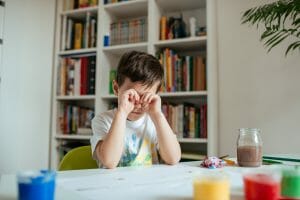 Tired child rubs his eyes. Boy losing concentration and getting tired after doing school painting assignments.