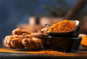 Turmeric powder and fresh turmeric on wooden background